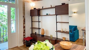A modern living room with exposed wooden beams, a built-in wooden shelving unit, a blue sofa, and a wooden dining table.