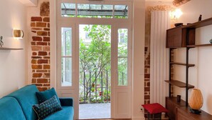 A room with a blue sofa, a wooden cabinet with shelves, and a door leading to a balcony with plants.