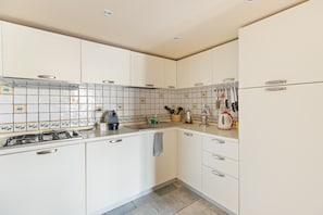 Una cucina con mobili bianchi, zoccolo in piastrelle e piano cottura a gas.