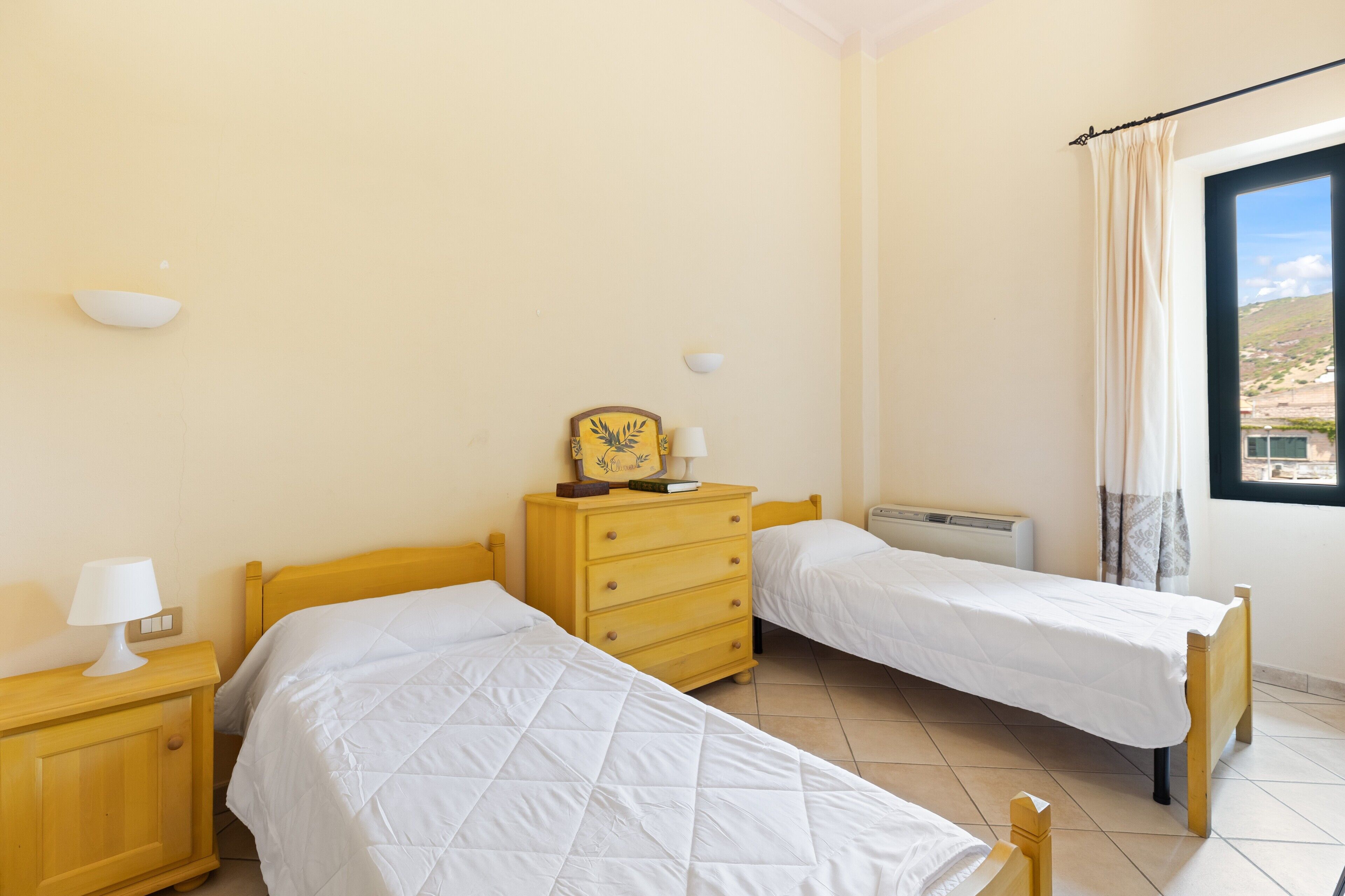 Une chambre avec deux lits, une commode, une lampe et une fenêtre donnant sur un beau paysage.
