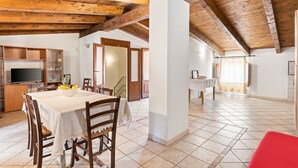 A dining area with a table, chairs, a TV, and a kitchen area with cabinets and a refrigerator.