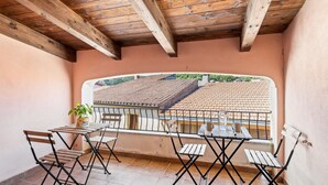 A balcony with wooden beams, a table, and chairs, overlooking a tiled roof.