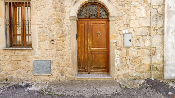 A stone building with a wooden double door, a window with metal bars, and a small electrical box on the wall.