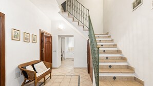 A staircase with a green railing, a wicker bench with cushions, and a tiled floor.