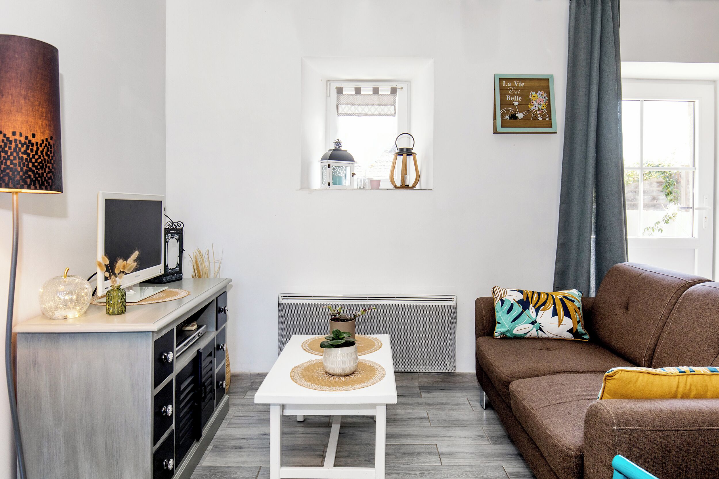 Un salon moderne avec une table blanche, un canapé marron et une fenêtre agrémentée d’objets décoratifs.