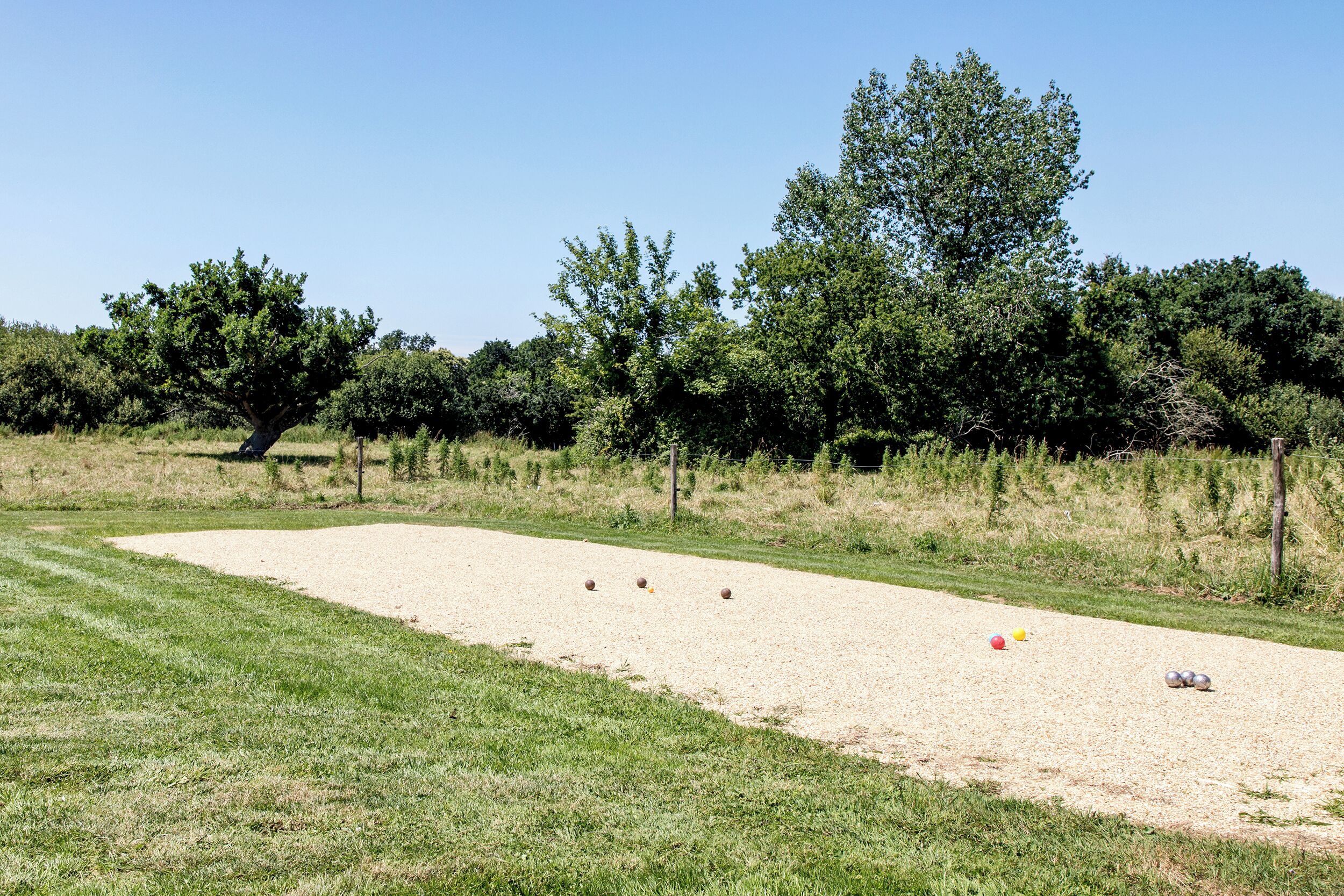 A sandy sports court with a grassy area, trees, and a clear sky.