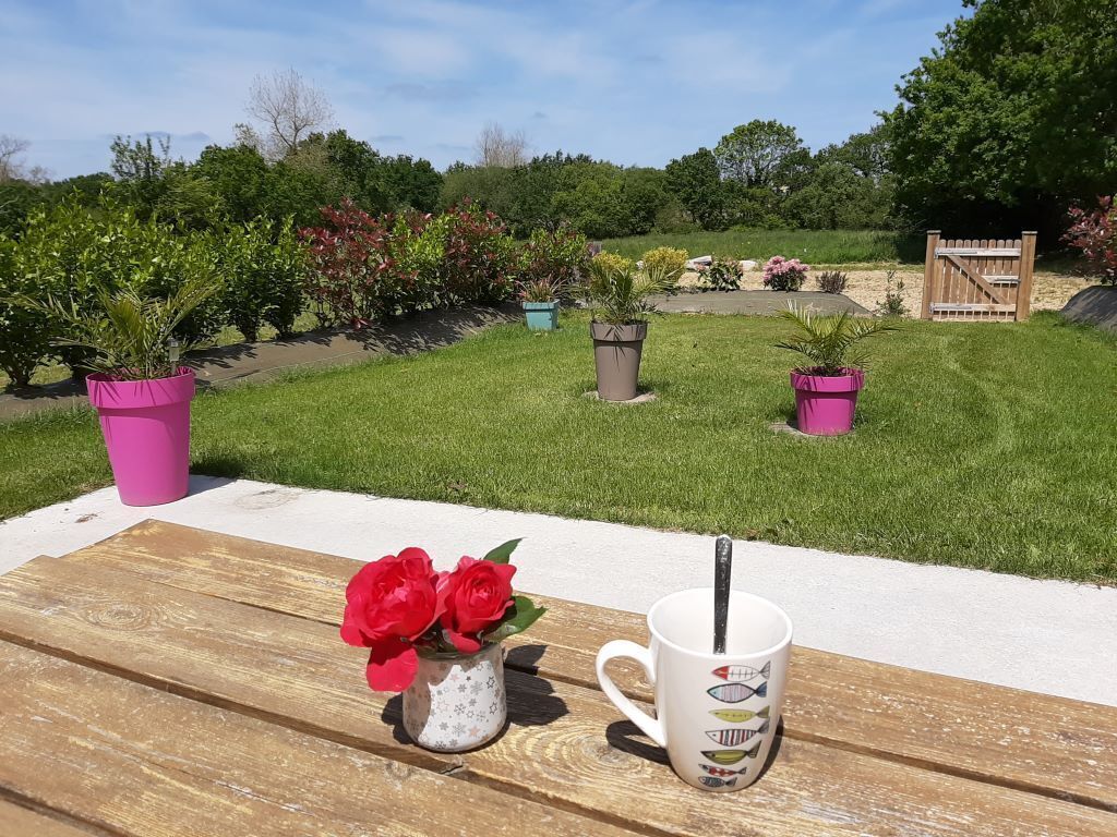 Une table en bois sur laquelle se trouvent une tasse blanche et un petit vase avec quelques fleurs rouges.