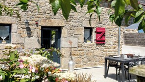Un edificio de piedra con un letrero rojo en forma de 'Z', mesas al aire libre y una planta en maceta.