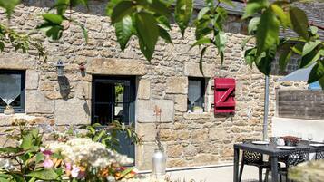 Un bâtiment en pierre avec une enseigne rouge en forme de « Z », des places assises à l’extérieur et un pot de fleurs.