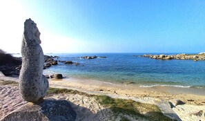 A coastal landscape with a prominent rock formation in the foreground, a sandy beach, and calm sea waters.