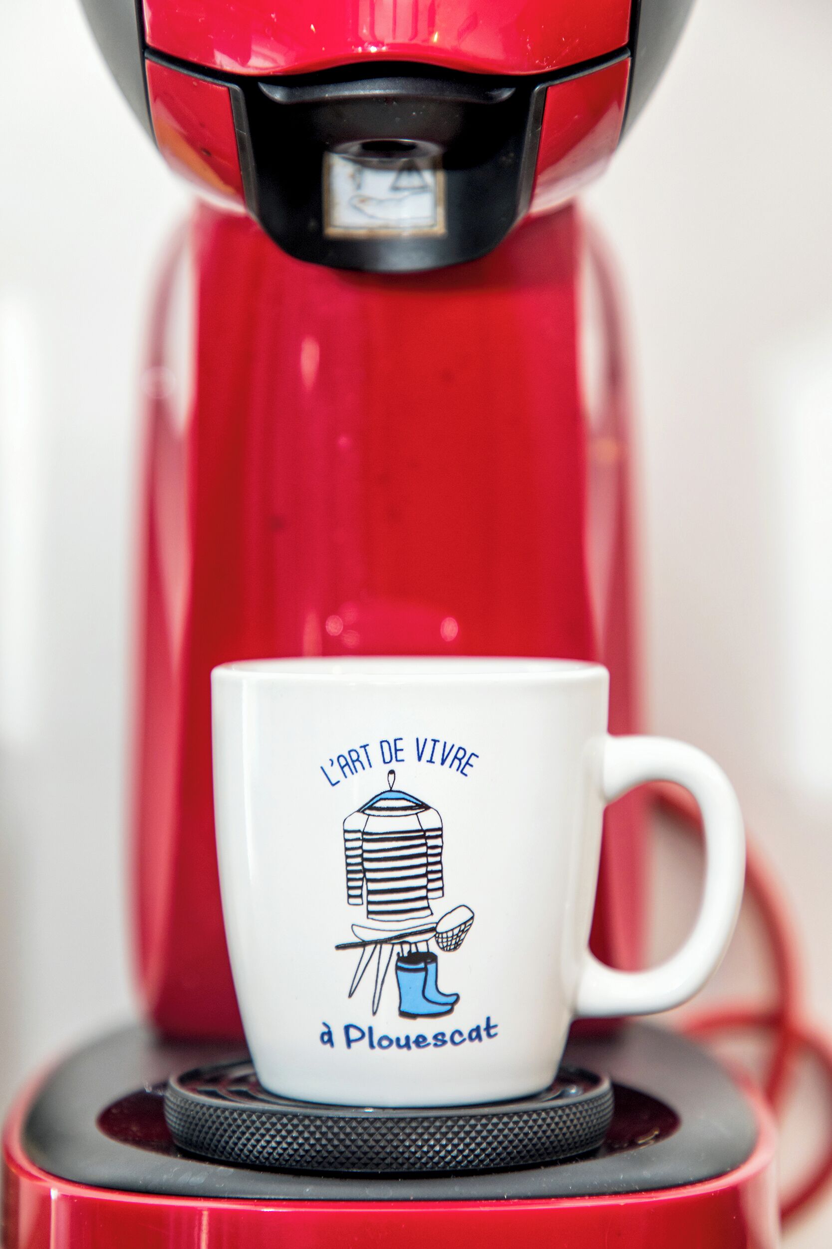 A red coffee maker with a white mug in front of it.