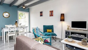 Una sala de estar con un sofá, un sillón verde azulado, un mueble para televisión y una zona de comedor con una mesa y sillas blancas.