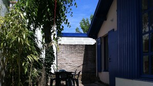 Ein Innenhof mit einem gepflasterten Weg, der zu einem blauen Gebäude führt, umgeben von Grünflächen und einem Tisch mit Stühlen.
