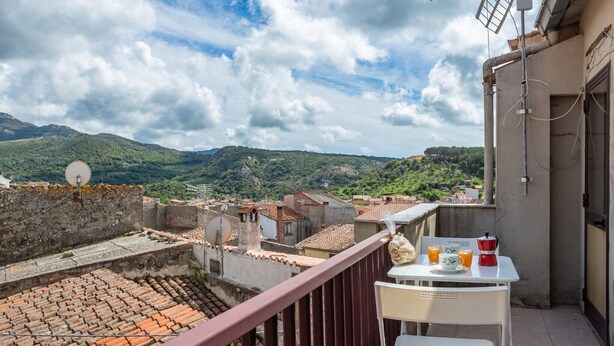 A balcony with a table, chairs, and a view of a cityscape and mountains.
