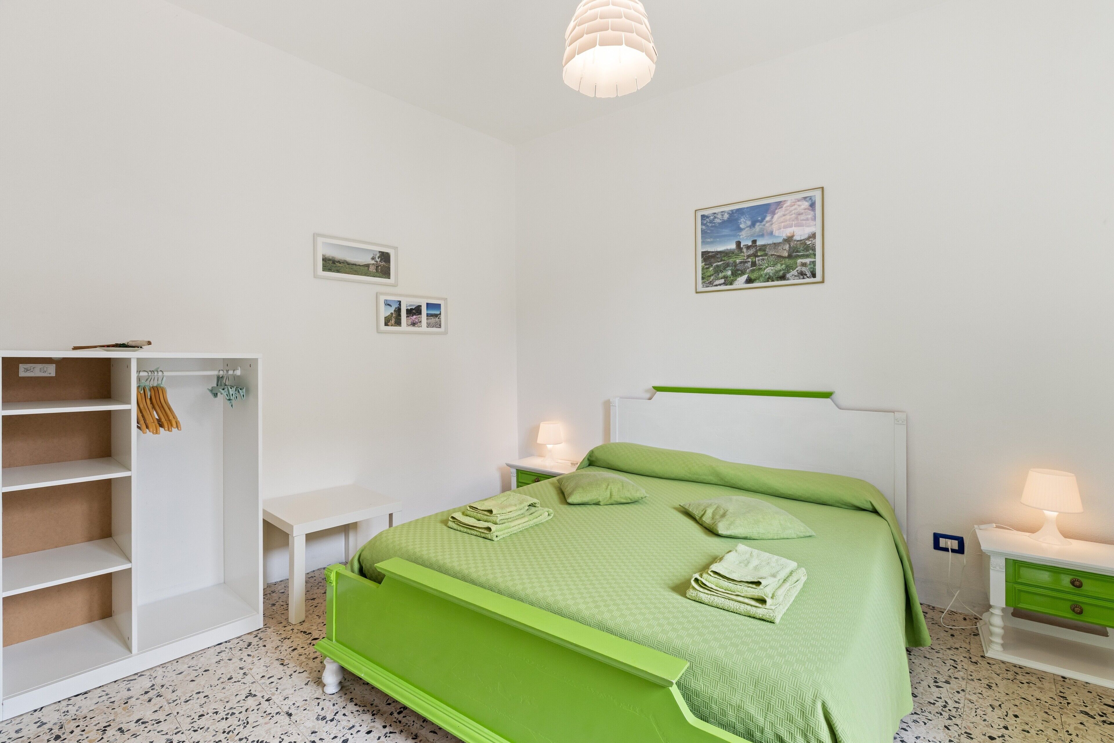 Ein Schlafzimmer mit einem grünen Bett, weißen Wänden, einem weißen Kleiderschrank und einem kleinen Nachttisch mit Lampe.