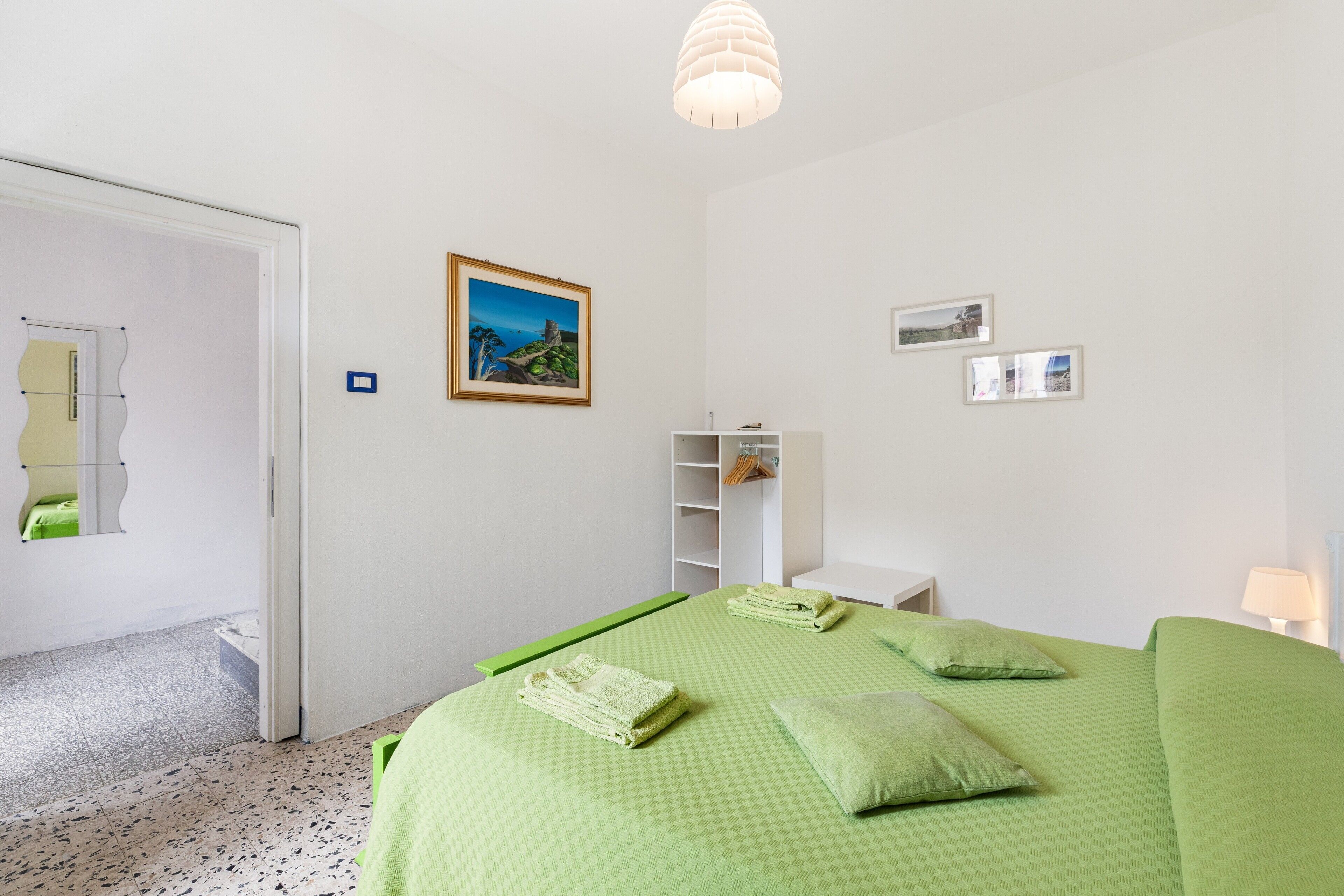 A bedroom with a bed, green bedding, a picture on the wall, and a white nightstand.