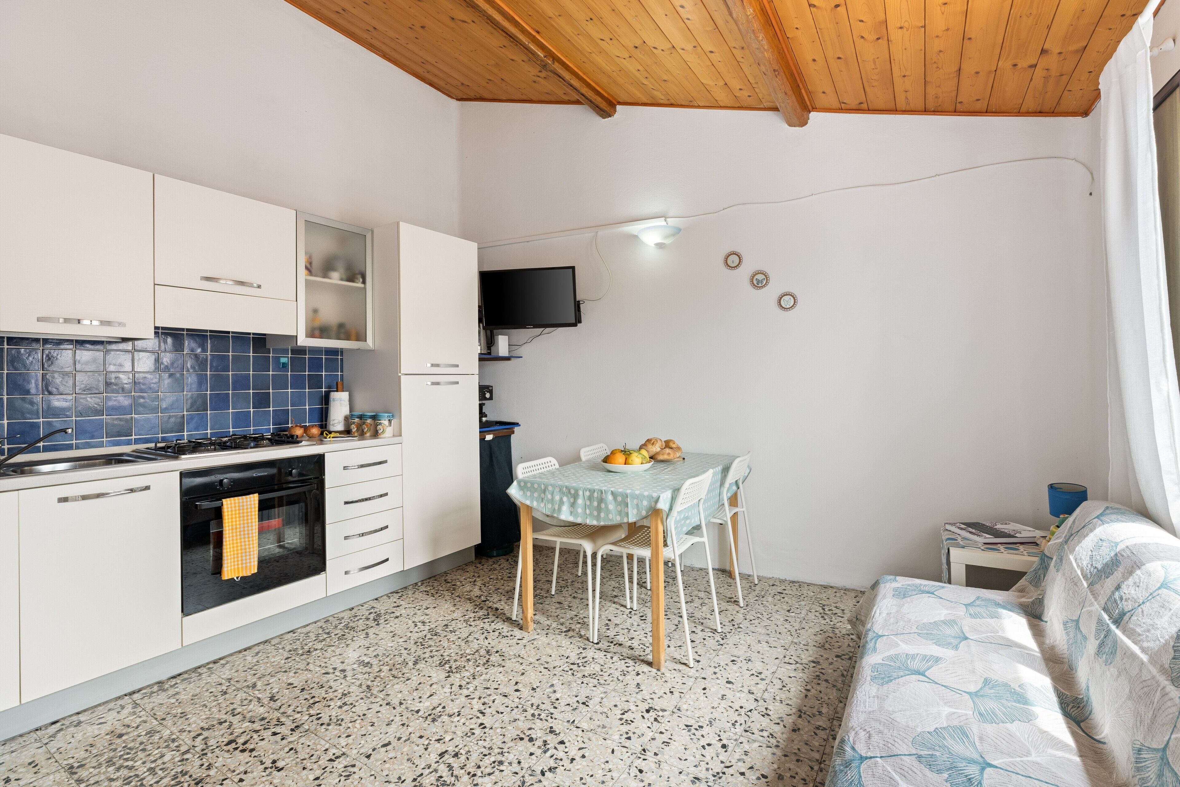 Cocina compacta con armarios blancos, estufa y comedor con mesa y sillas.