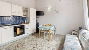 A compact kitchen with white cabinets, a stove, and a dining area with a table and chairs.