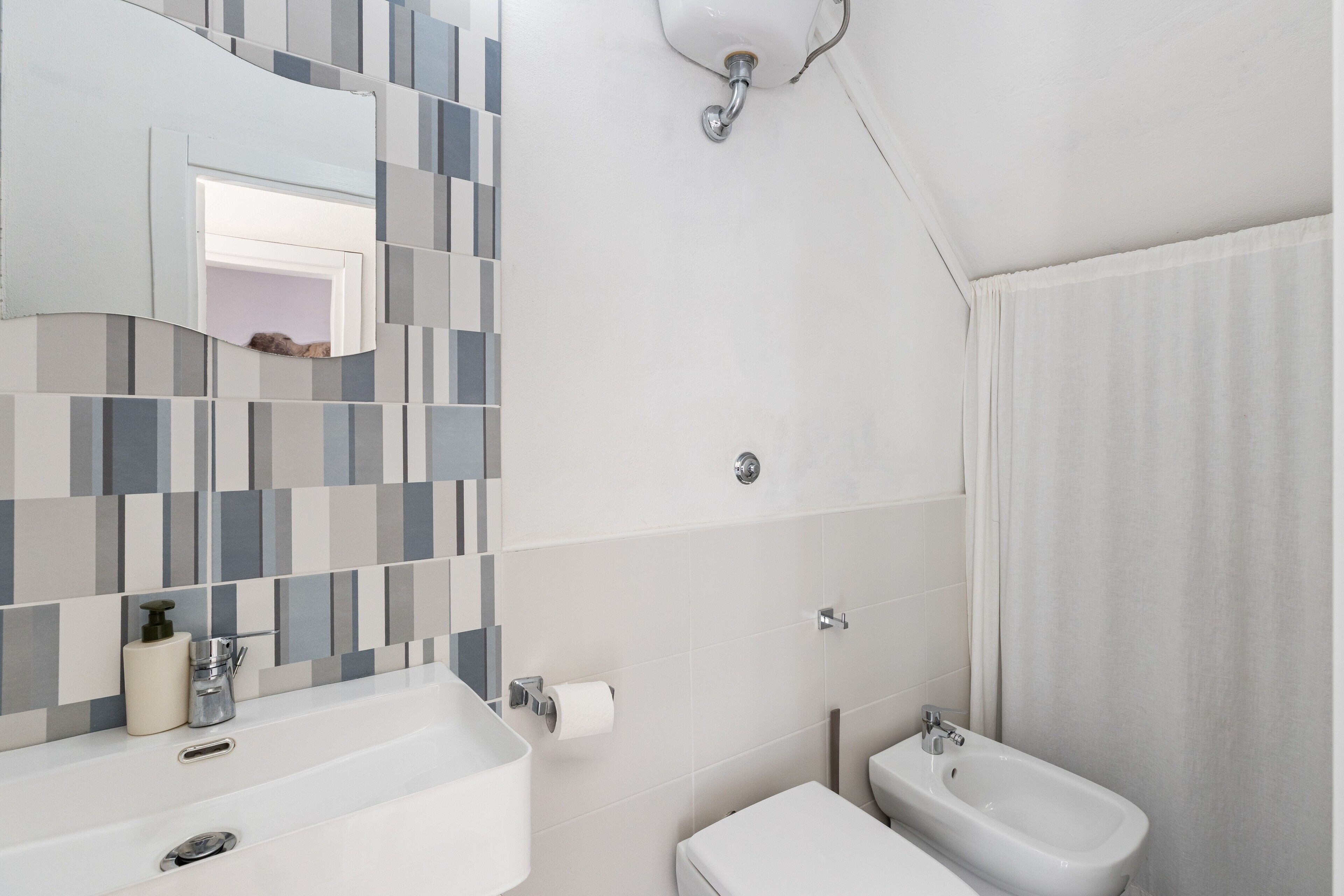 A bathroom with a tiled wall, a sink, a bidet, and a mirror.