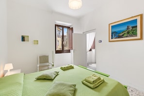 A bedroom with a bed, pillows, a painting, a window, and a door leading to another room.
