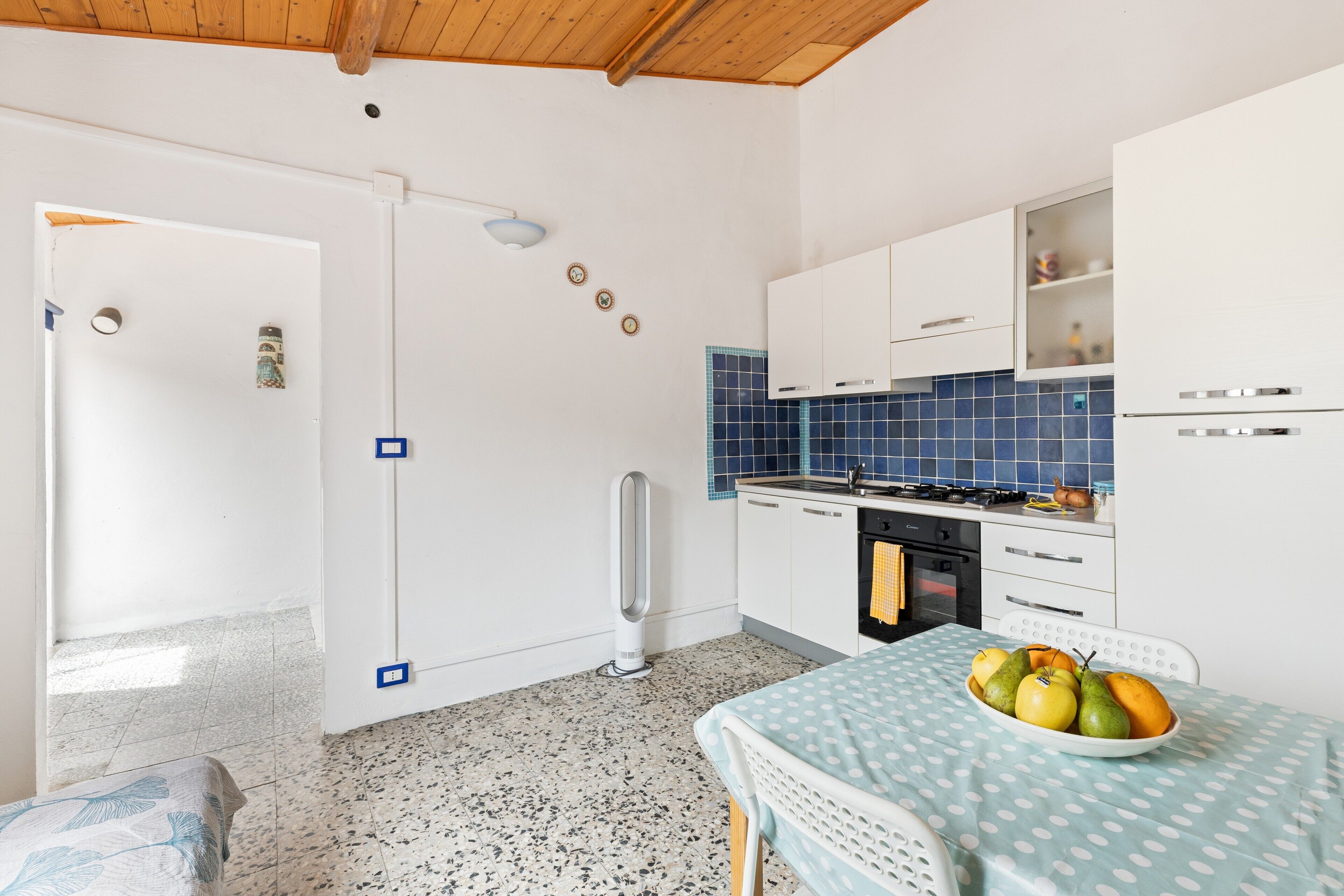 Une cuisine avec des meubles blancs, une cuisinière et une table à manger sur laquelle se trouve un panier de fruits.