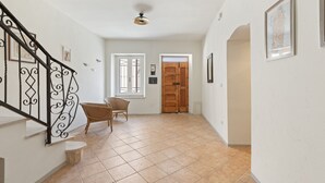 A hallway with a staircase, a wicker chair, and a wooden door.