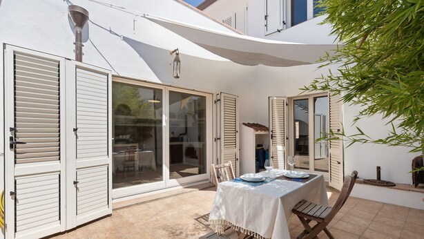 A patio with a table set for dining, a chair, and a lamp.