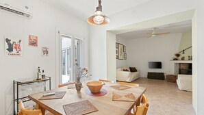 A dining area with a wooden table, chairs, a hanging light fixture, and a wall-mounted TV.