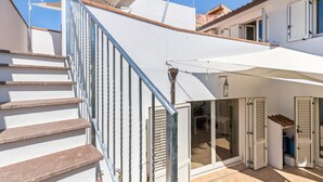 A residential building with a staircase, sliding glass doors, and a covered patio area.