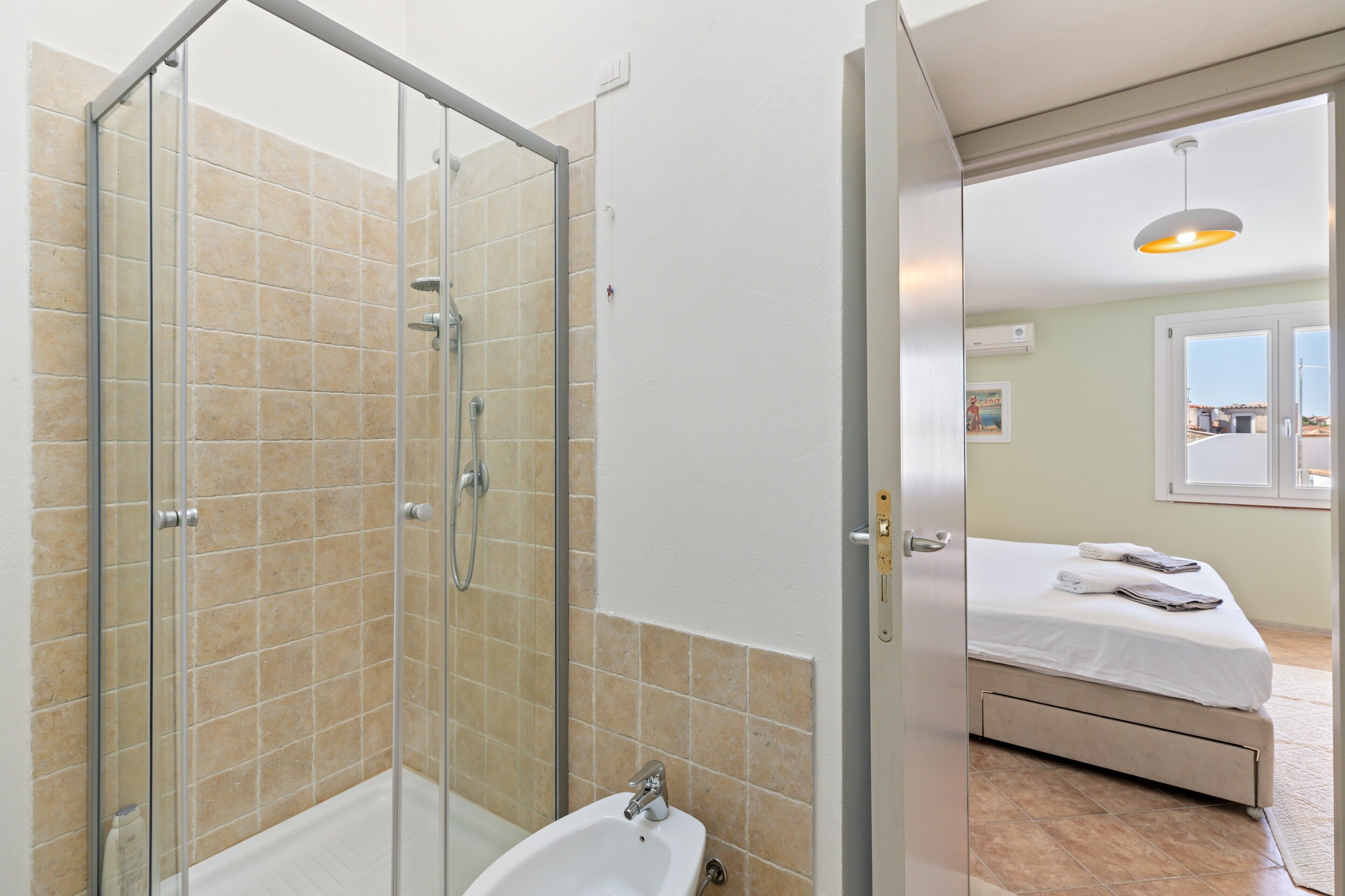 Un baño con cabina de ducha de vidrio, un lavabo y una cama en la habitación contigua.