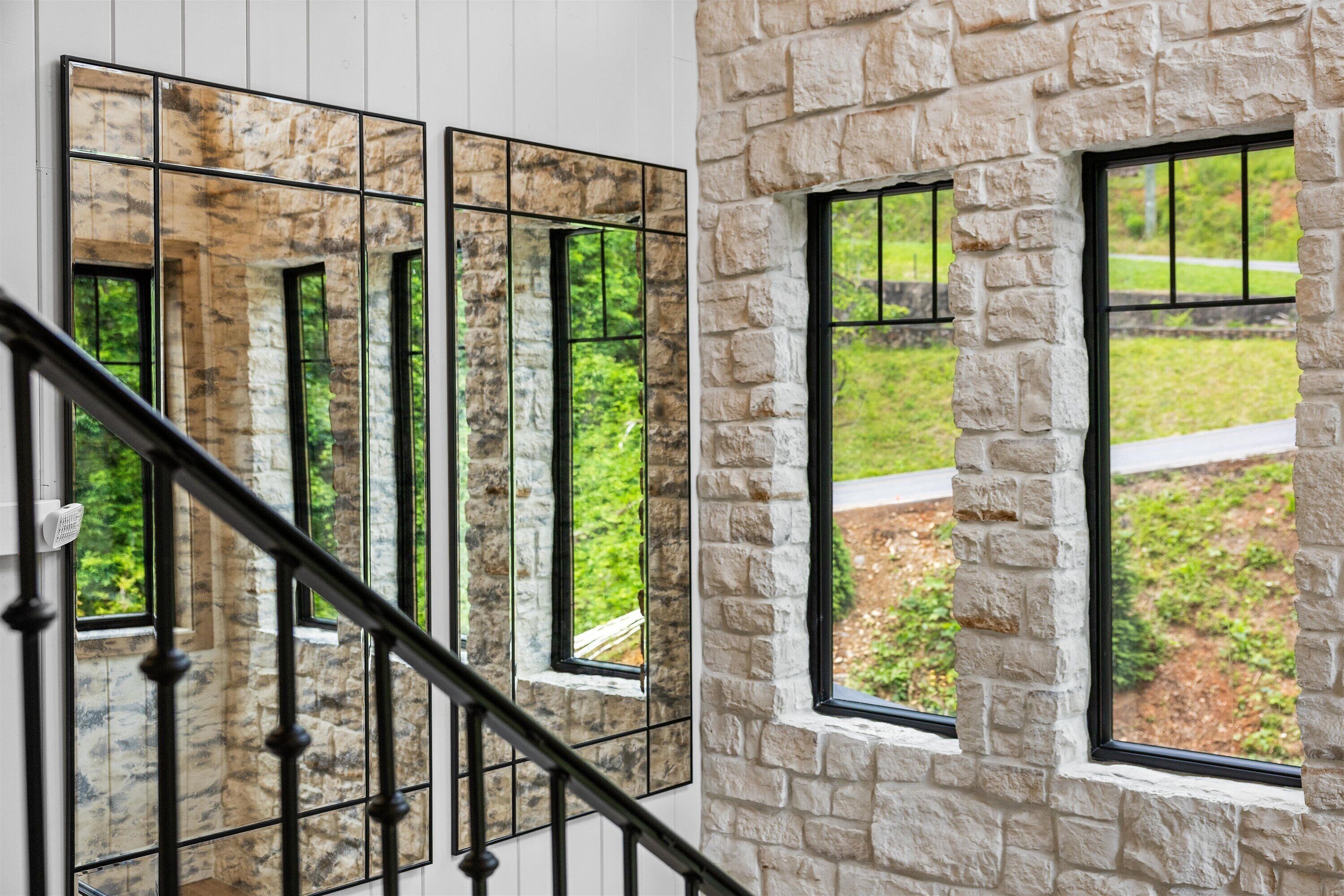 Una escalera con barandilla, un muro de piedra y ventanas que dan a zonas verdes.
