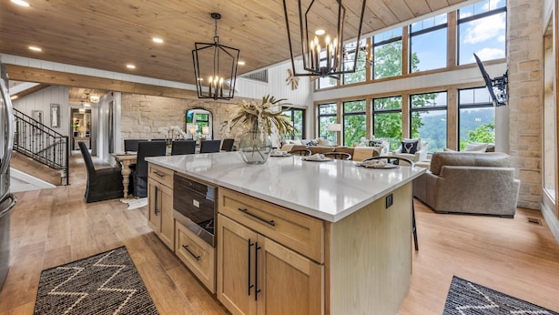 A spacious kitchen with a large island, wooden ceiling, and large windows offering views of the outdoors.