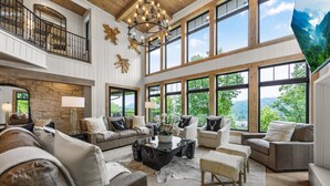 A spacious living room with high ceilings, large windows, and a stone fireplace.
