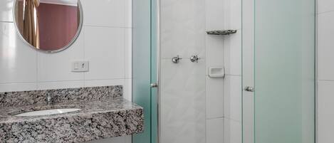 A bathroom with a glass-enclosed shower, a marble sink, and a round mirror.