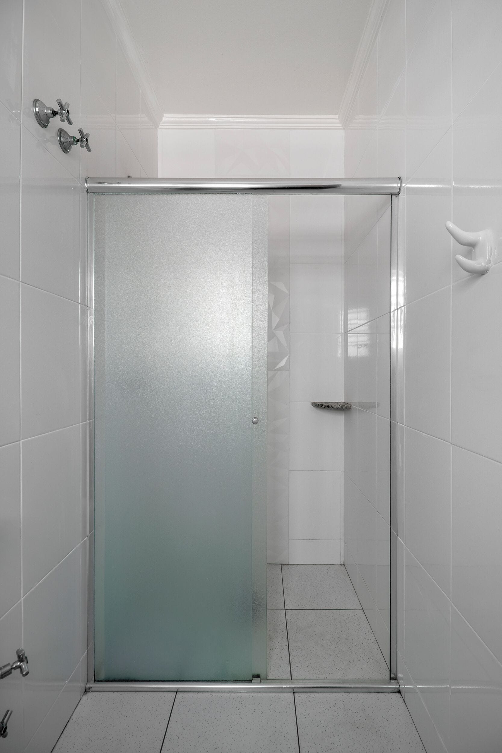 Ein Badezimmer mit weiß gefliesten Wänden, einer Duschkabine aus Glas und einem weißen Handtuchhalter.