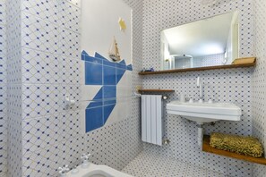 A bathroom with patterned tiles, a white sink, a mirror, and a ship decoration on the wall.