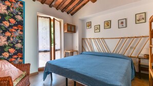 A bedroom with a bed, a chair, a wooden headboard, a window with curtains, and a wall with framed pictures. - Villa 'I Fiori Redinoce' with Private Terrace, Private Garden, and Air Conditioning (Procchio)