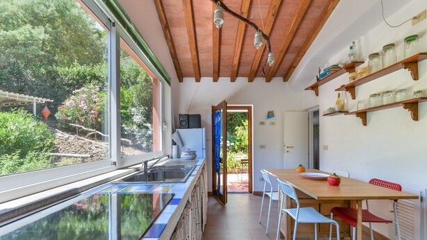 A kitchen with a glass backsplash, wooden ceiling beams, and a dining area with a wooden table and chairs. - Villa 'I Fiori Redinoce' with Private Terrace, Private Garden, and Air Conditioning (Procchio)