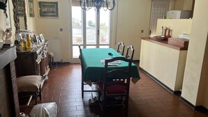 Un coin repas avec une table verte, des chaises en bois, un lustre et une vue à travers une porte vitrée.