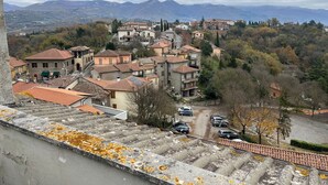 Un village perché sur une colline, avec des maisons à étages, une route pavée et une vue sur les montagnes lointaines.