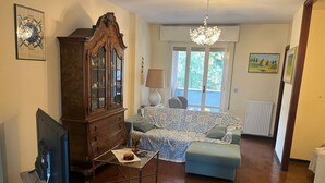 Un salon avec un meuble en bois, un téléviseur posé sur un meuble, un canapé à motifs et un lustre.