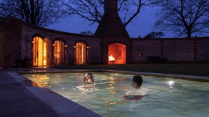 A swimming pool with two people in it, surrounded by brick walls and arched windows. - Wilderness Reserve - The Grange (Halesworth)