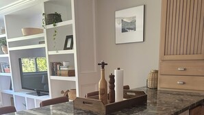 Een keuken met een marmeren aanrechtblad, houten kastjes, een inbouwvaatwasser en een raam met uitzicht op groen.