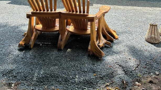Een houten Adirondack-stoel en tafel staan op grind voor een gebouw met een overdekte veranda.