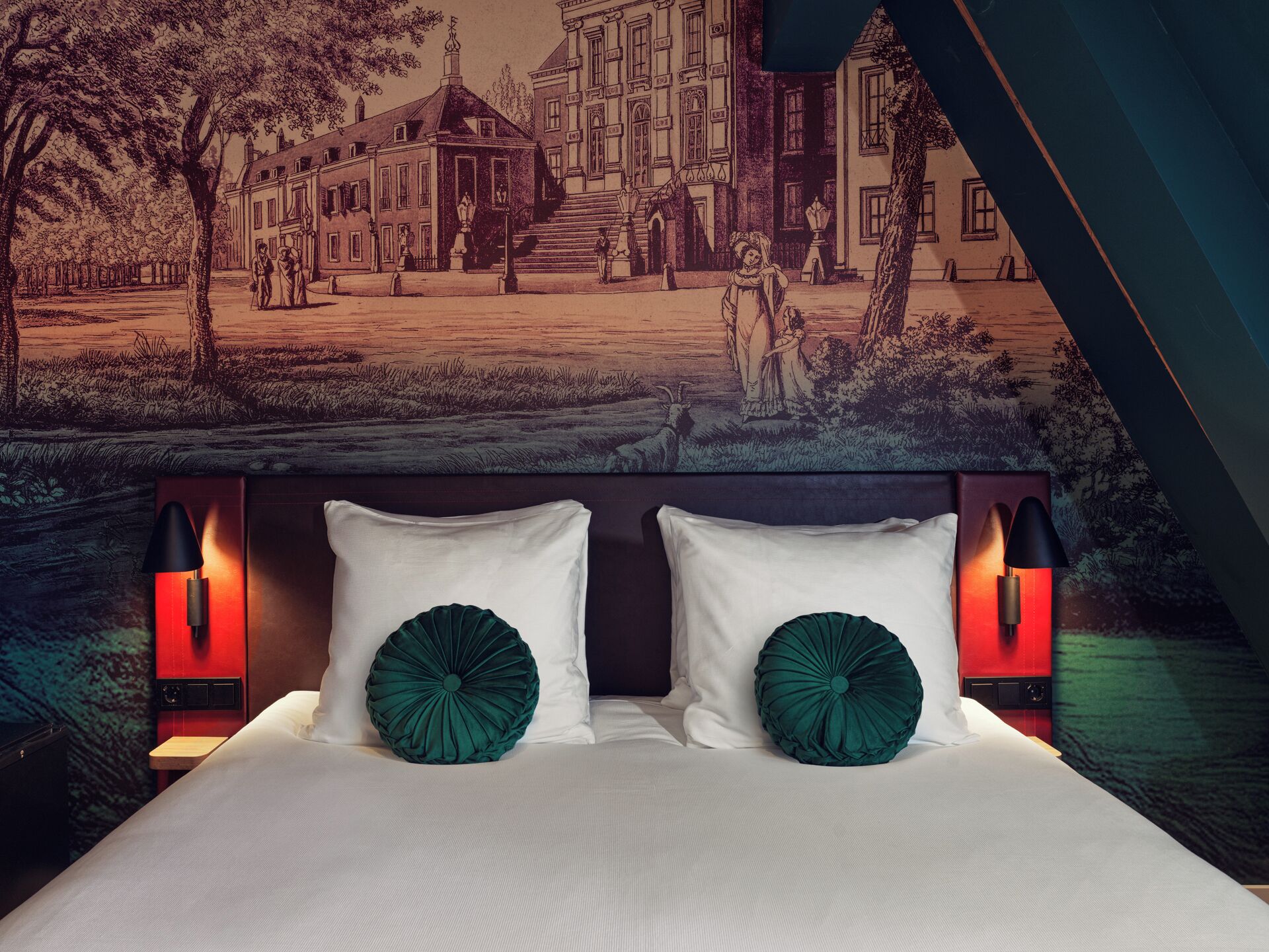 A bedroom with a large bed, two white pillows, two green decorative pillows, and two wall-mounted lamps.