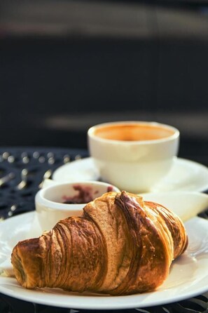 En croissant på en vit tallrik, med en kopp kaffe i bakgrunden.