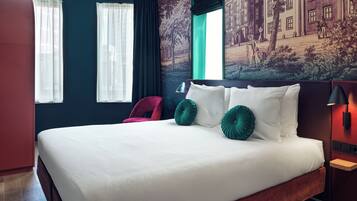 Une chambre d’hôtel avec un grand lit, un fauteuil rouge, une table de chevet avec une lampe et une fresque murale.