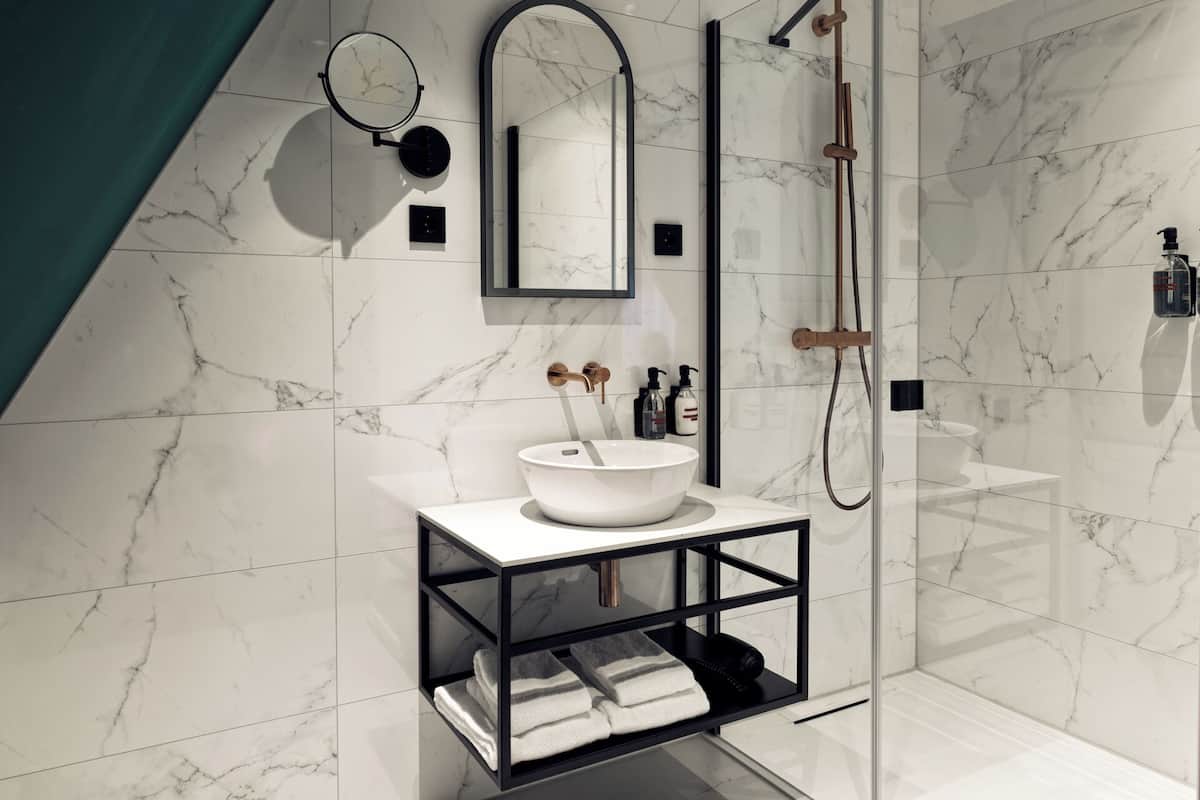 A modern bathroom with a white marble floor, a white sink with a black frame, a glass shower enclosure, and a mirror with a black frame.