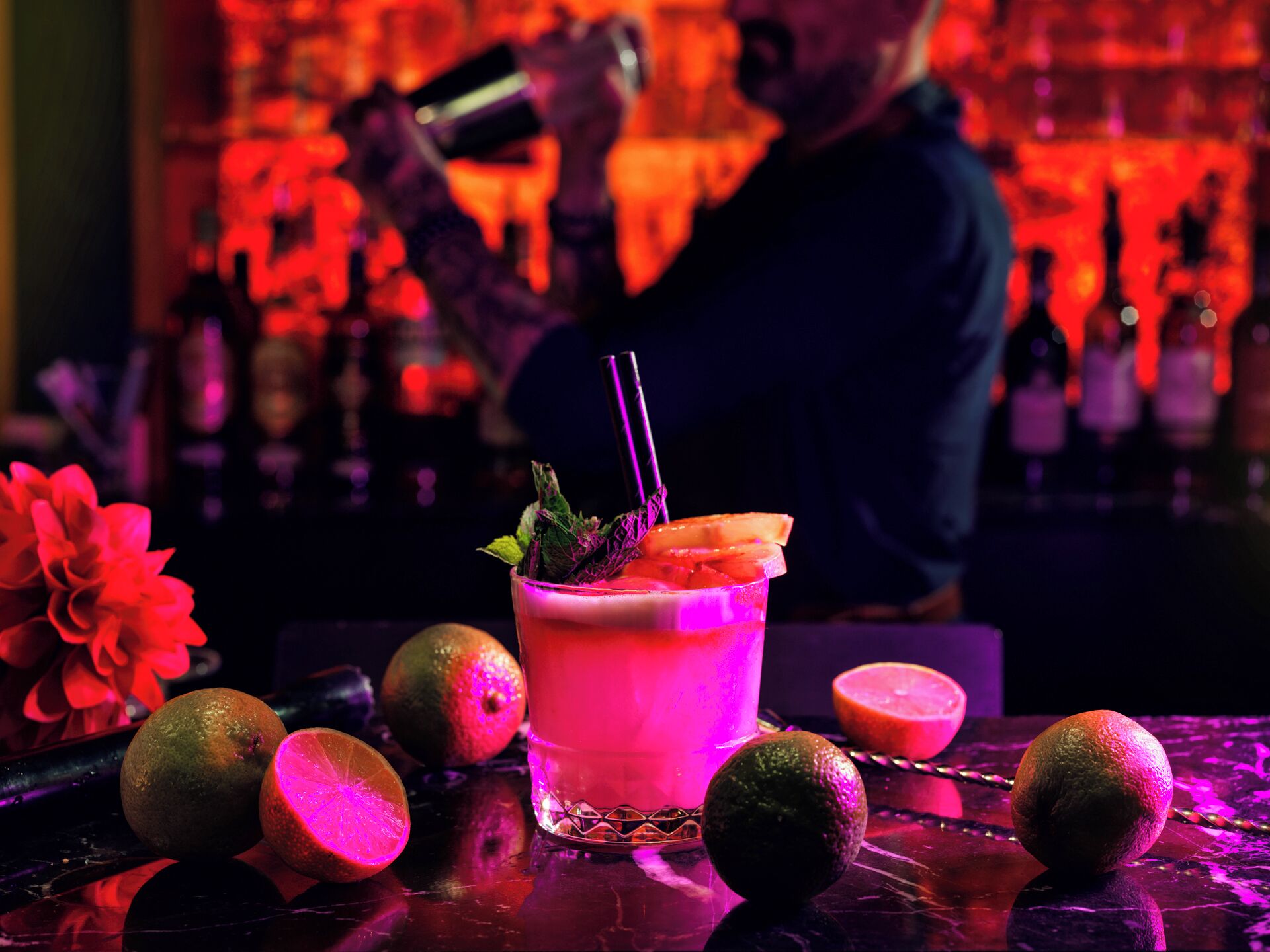 A bar setting with a cocktail, lime, and a bartender.