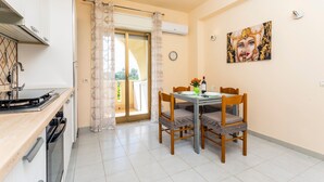Una cocina con estufa, horno y lavavajillas, una mesa de comedor con sillas, una puerta corrediza de vidrio y un reloj en la pared.